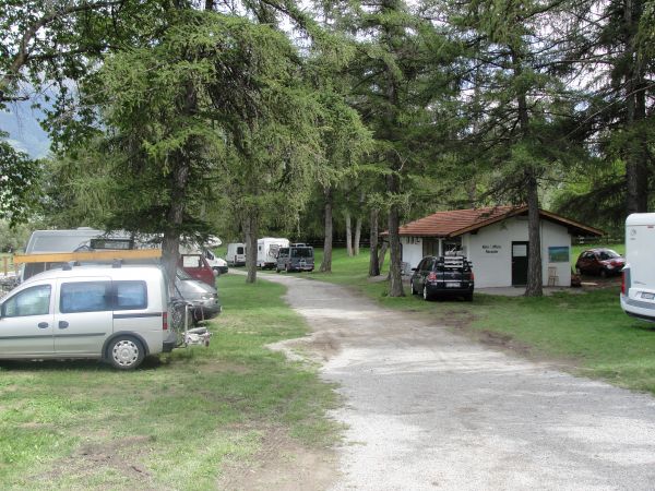 Un campeggio con auto e camper tra gli alberi vicino a un edificio con tetto rosso.