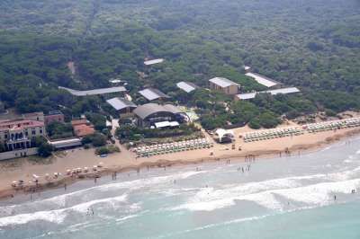 Spiaggia con bagnanti e ombrelloni, circondata da vegetazione fitta e alcuni edifici.