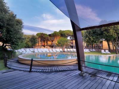 Una piscina circondata da sdraio su una terrazza in legno, con alberi attorno.