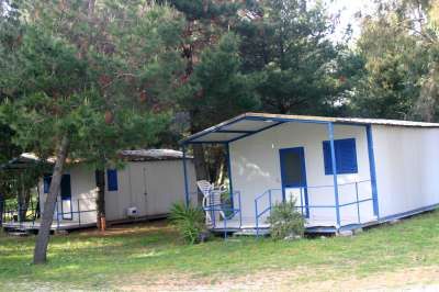 Due bungalow bianchi con porte e finestre blu, immersi tra gli alberi.