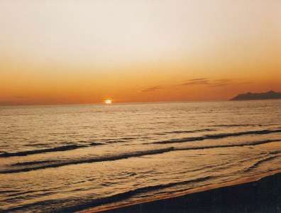 Tramonto sul mare con onde leggere e profilo di una montagna all'orizzonte.