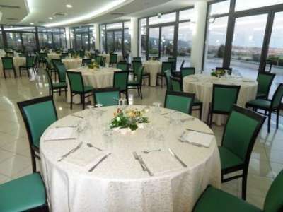 Sala da pranzo con tavoli rotondi apparecchiati e sedie verdi, vista sulle finestre.