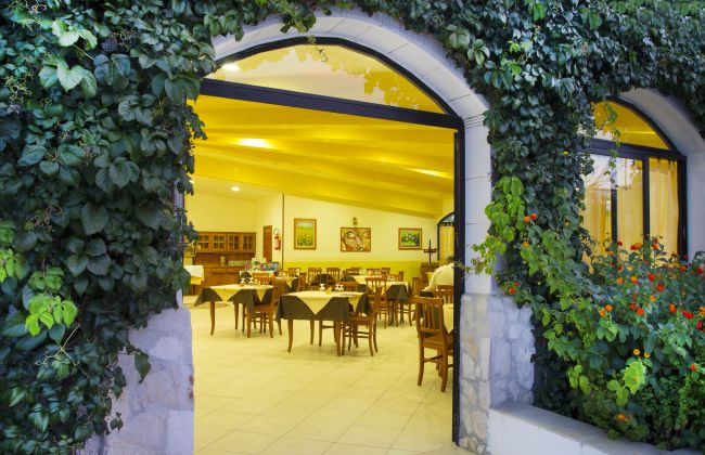 Entrata di un ristorante con vetrata e piante rampicanti.