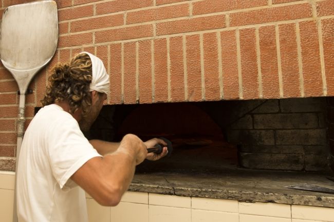Un uomo inserisce una pala in un forno a legna.