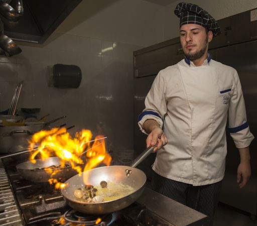 Cuoco in cucina con fiamma alta.