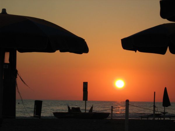 Tramonto visto da una spiaggia con ombrelloni.