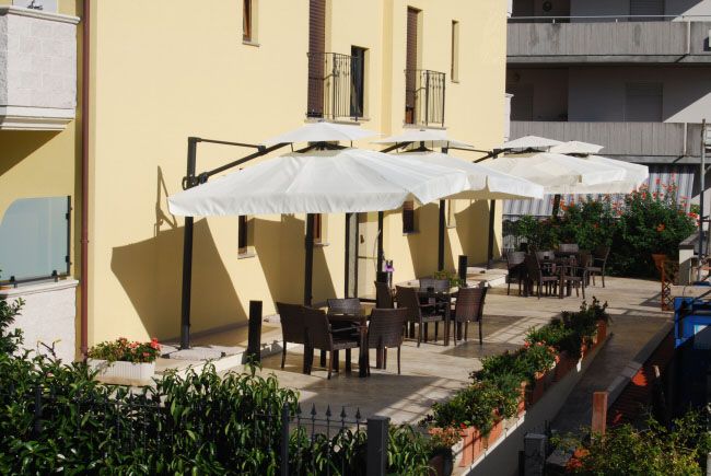 Terrazza con tavoli e sedie ombreggiati da grandi ombrelloni bianchi.