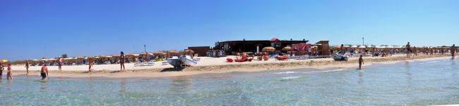 Spiaggia con barca sulla sabbia, molti ombrelloni e bagnanti in acqua.