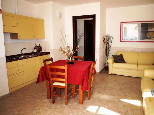 Cucina con tavolo rosso, sedie in legno, divano giallo e mobili gialli.