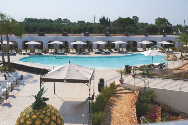 Piscina con lettini e ombrelloni, circondata da vegetazione e vialetti.
