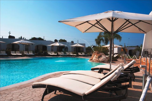 Lettini con ombrelloni accanto a una piscina azzurra all'aperto.