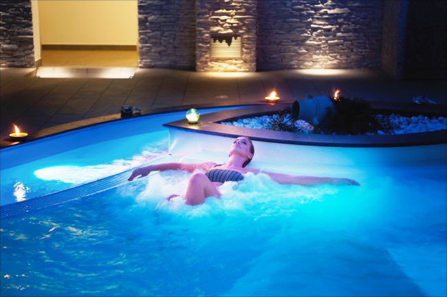 Persona rilassata in una piscina con illuminazione blu e candele attorno.