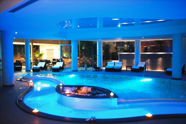 Piscina illuminata di blu in un ambiente interno elegante con lettini.