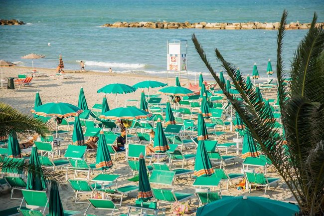 Spiaggia con ombrelloni verdi e mare azzurro.