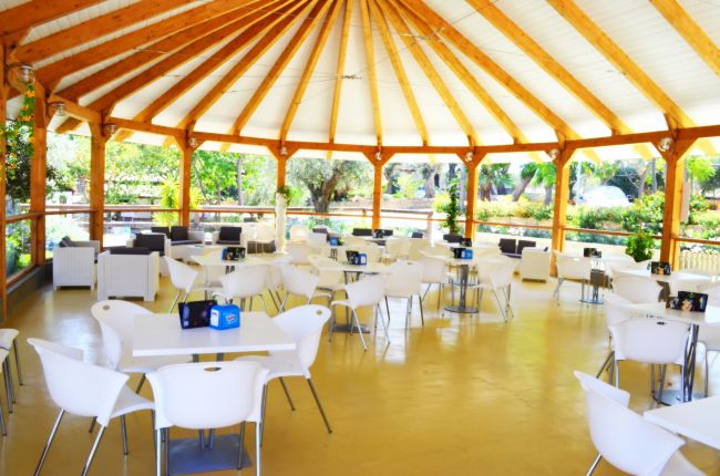 Gazebo con tavoli bianchi e sedie, circondato dal verde.