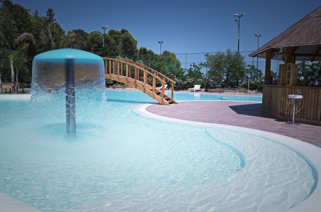 Piscina con fontana a ombrello e ponticello in legno.