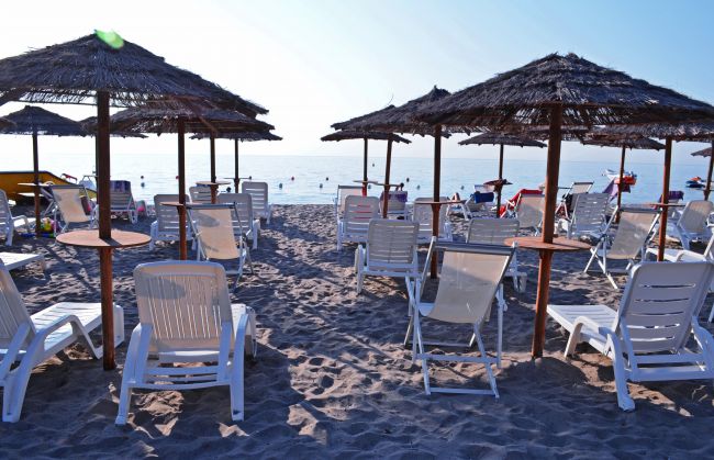 Spiaggia con sedie a sdraio e ombrelloni di paglia.