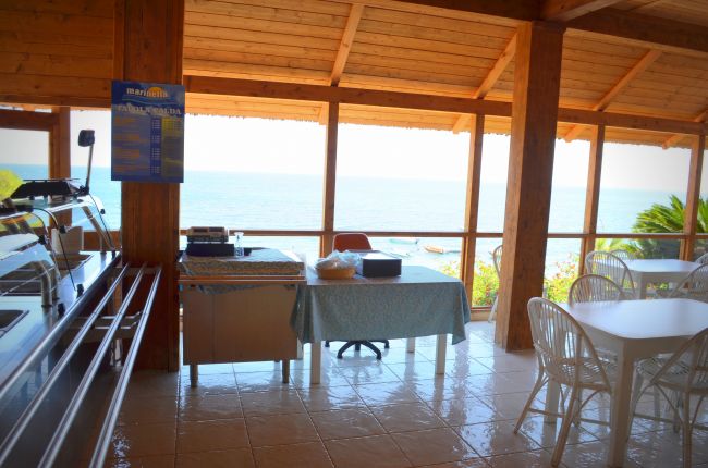 Sala da pranzo con vista mare, tavoli e sedie bianche.