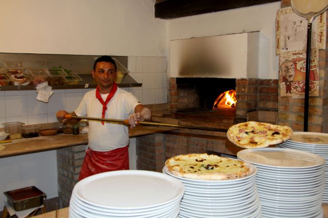 Pizzaiolo estrae pizza da forno a legna.