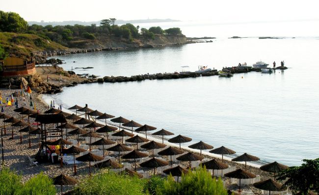 Spiaggia con ombrelloni e molo sul mare.