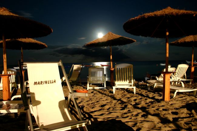 Spiaggia notturna con luna piena e ombrelloni.