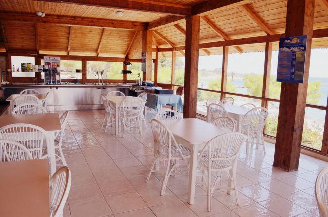 Sala luminosa con tavoli e sedie bianche, vista esterna.