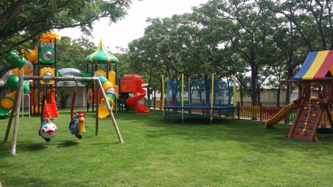 Parco giochi colorato con altalene e scivoli tra gli alberi.
