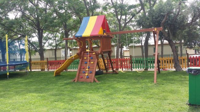 Parco giochi con scivolo e altalene in un prato.