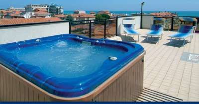 Una terrazza con jacuzzi blu e lettini, vista mare.