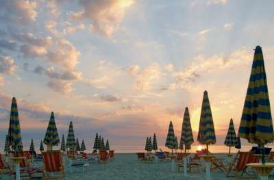 Ombrelloni colorati in spiaggia al tramonto con cielo parzialmente nuvoloso.