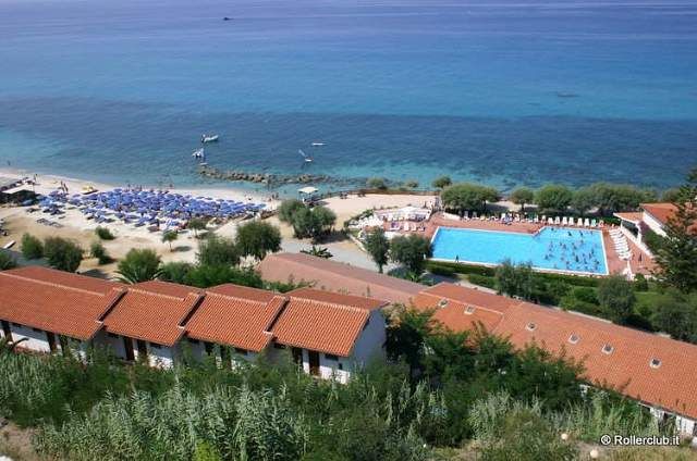 Spiaggia e villaggio con piscina vista dall'alto, ombrelloni disposti lungo la costa.