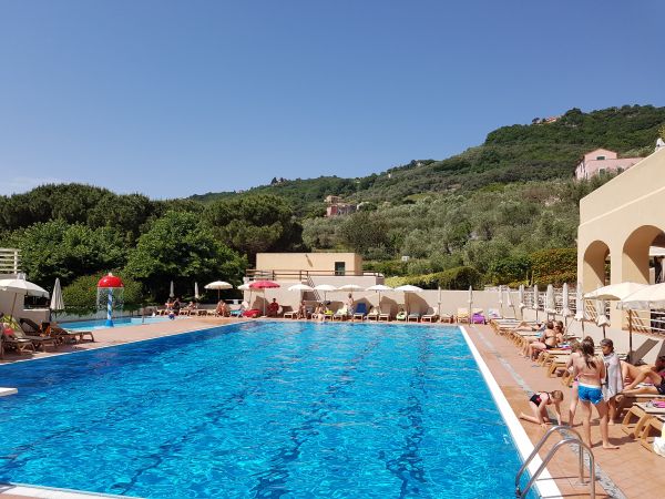 Piscina all'aperto con bagnanti, circondata da colline verdi.