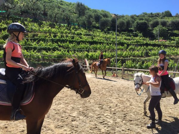 Bambini a cavallo in un campo recintato con colline verdi sullo sfondo.