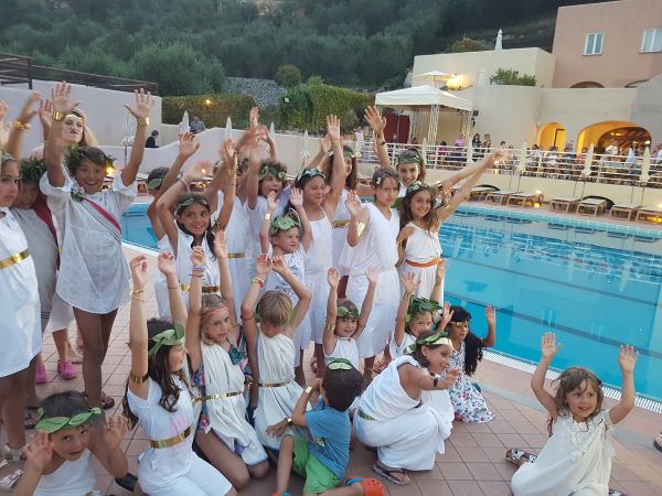 Bambini in abiti bianchi festeggiano accanto a una piscina.