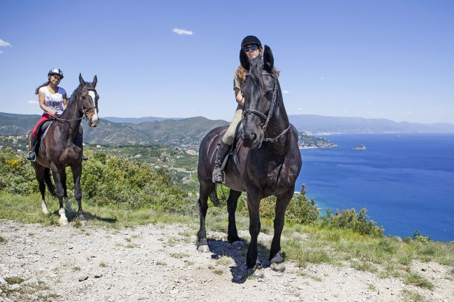 Due persone a cavallo su un sentiero con vista mare.
