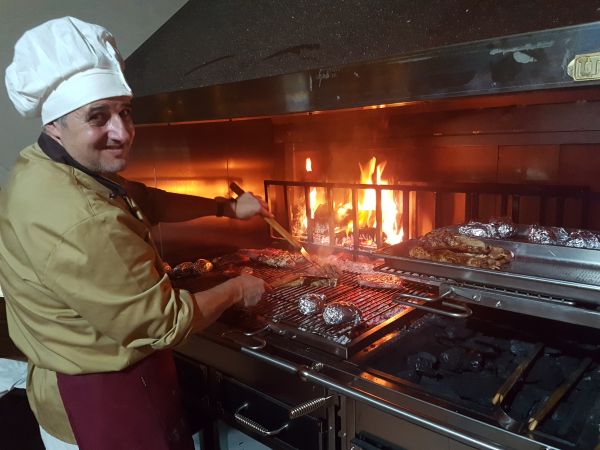 Cuoco che griglia davanti a un fuoco vivo.
