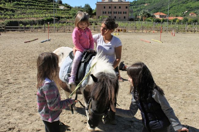 Bambini accarezzano un pony mentre una bambina è in sella sotto la supervisione di un adulto.