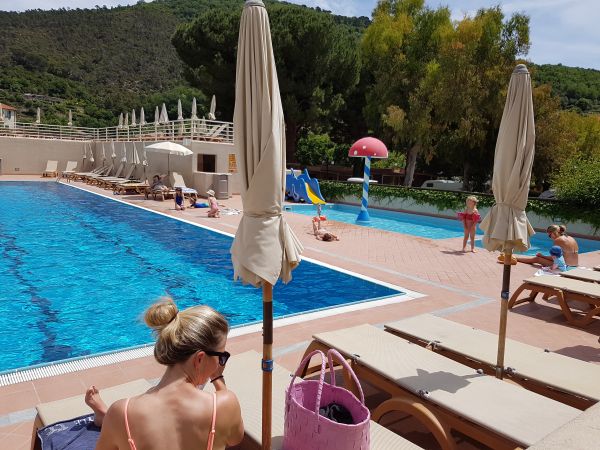Una piscina con lettini e ombrelloni, persone che si rilassano.