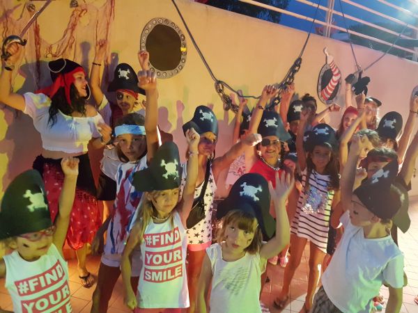 Bambini in costumi da pirata alzano le mani, sorridendo.