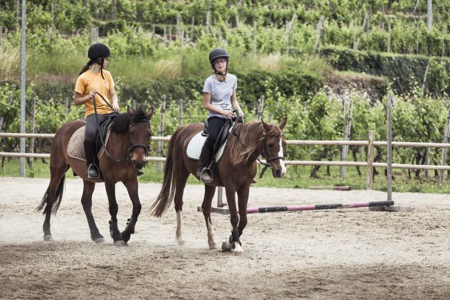 Due persone a cavallo in un'area esterna con recinzione.