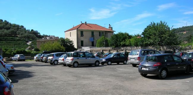 Parcheggio pieno di auto vicino a una casa con tetto rosso.