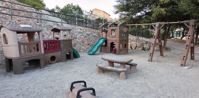Parco giochi con scivoli, altalene e tavolo da picnic su sabbia.