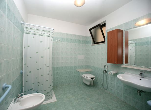 Bagno con piastrelle verdi, doccia con tenda, lavandino e WC.
