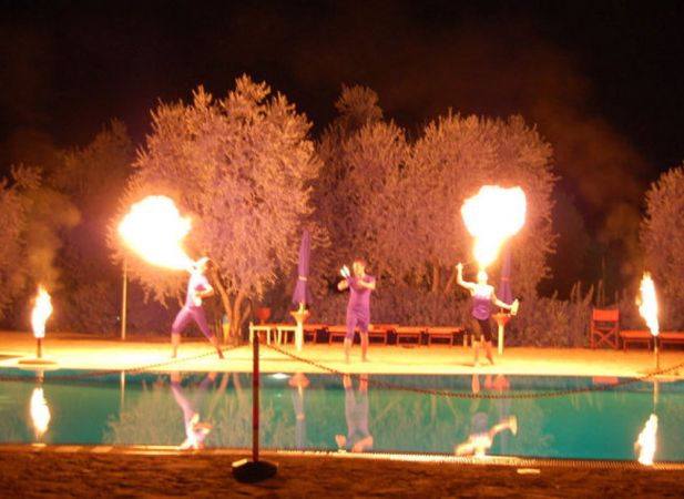 Spettacolo notturno di giocolieri col fuoco vicino a una piscina.
