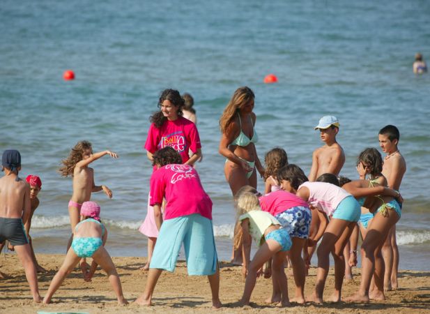 Bambini e adulti giocano sulla spiaggia con il mare sullo sfondo.