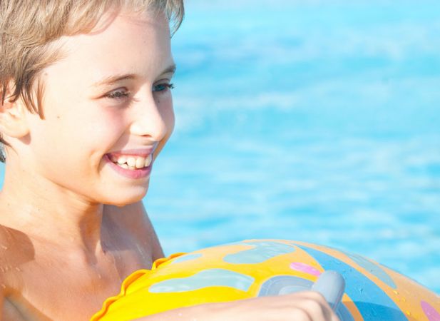 Bambino sorridente in piscina con un galleggiante colorato.