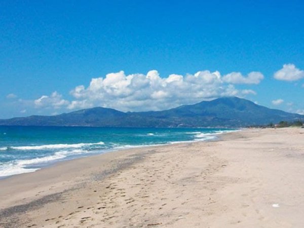 Spiaggia sabbiosa con mare azzurro e montagne in lontananza.