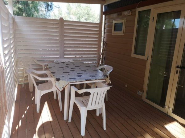 Terrazza in legno con tavolo, sedie bianche e pareti a persiana.