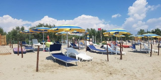 Spiaggia con lettini blu e ombrelloni gialli.