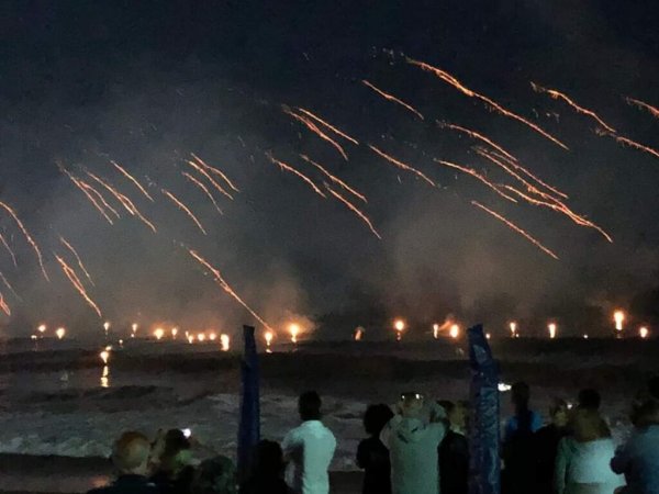 Fuochi d'artificio sul mare di notte con spettatori.